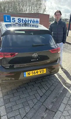 Geslaagde leerling in donkere jas naast de zwarte lesauto