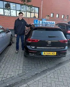 Geslaagde leerling in zwarte hoodie naast de lesauto