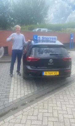 Geslaagde leerling in lichte trui naast de zwarte lesauto