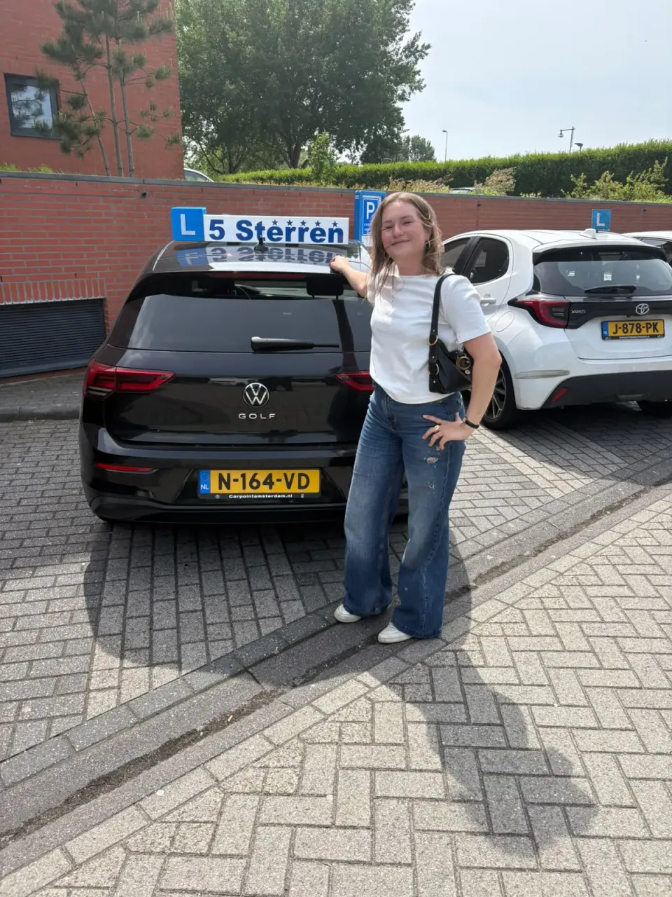 Geslaagde leerling in wit shirt wijst naar het lesbord op de lesauto