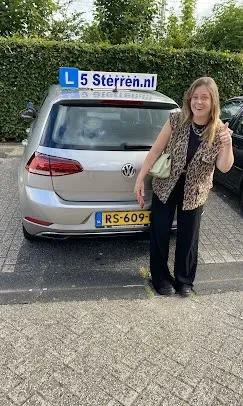 Geslaagde leerling in luipaardprint vest naast de zilveren lesauto